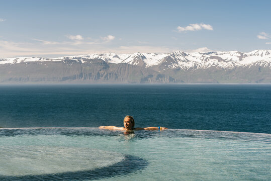 Side view os male tourist leaning on poolside and admiring majestic landscape of mountain ridge and tranquil sea