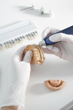 From above of crop anonymous dentist in medical gloves grinding dental prosthesis with professional tool while working in modern laboratory