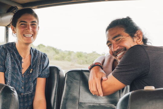 Fototapeta Side view of multiethnic couple sitting looking at camera in automobile and enjoying safari during summer vacation