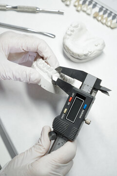 From above of crop anonymous orthodontist using caliper for measuring while working with model of dental jaw in laboratory