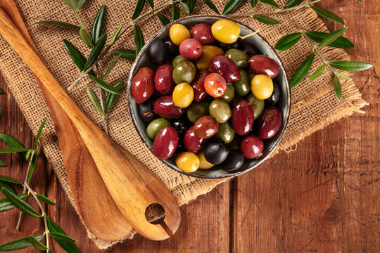 Olives. A variety of green, black and red olives, with leaves, shot from above on a rustic wooden background with a place for text