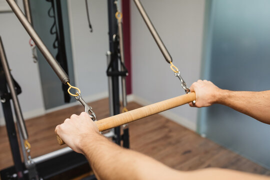 Unrecognizable male athlete exercising with wooden horizontal bar of pilates reformer in contemporary gym