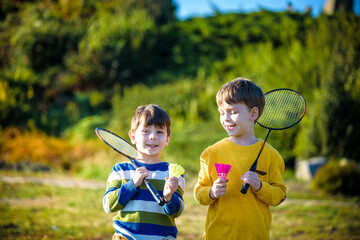 Active preschool girl and boy playing badminton in outdoor court in summer. Kids play tennis....