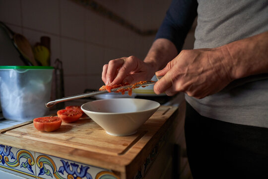 Stock photo of the detail of hands of a man grating tomato on top of a piece of wood in a kitchen