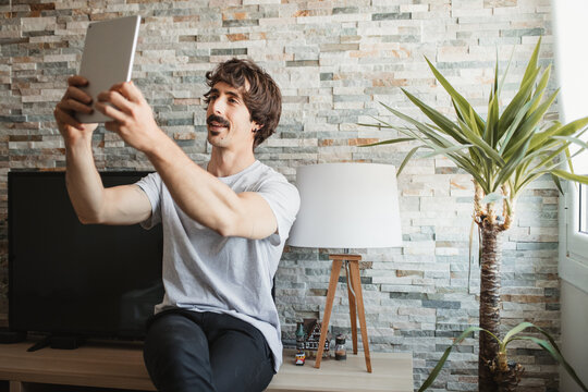 Relaxed male in casual wear sitting making video call on tablet while enjoying weekend at home