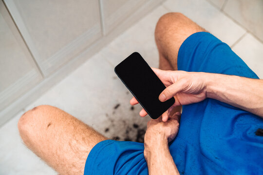 From above back view of crop shirtless male focusing on screen and watching tutorial video after self cutting hair in light bathroom at home as concept bad decisions or result of self isolation