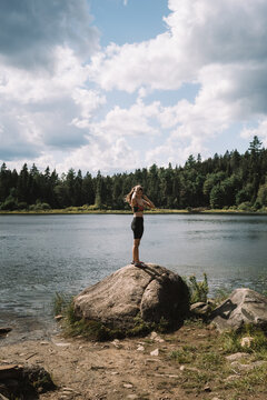 Side view of female traveler standing on stone on shore of calm rive on cloudy day in La Mauricie National Park in Quebec, Canada