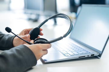 Rear view of the call center operator's desktop. Close-up of female hands with a headset over a laptop. Unrecognizable woman working in a support service took off her headphones.