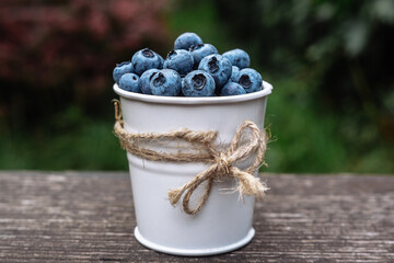 Some blueberries in a decorate small bucket on wooden banch in the garden on summer sunset