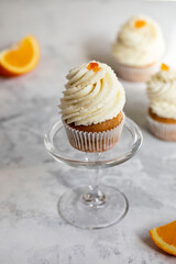 Homemade orange muffins with white cream, on a white and gray background.