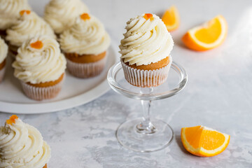Homemade orange muffins with white cream, on a white and gray background.