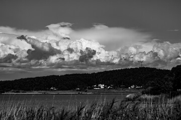 Storm clouds formation over a wooded area and a sea cove in black and white photograph