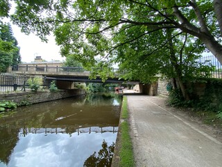 A bridge, crossing over the Leeds to Liverpool canal, with a boat in the distance in, Saltaire, Braford, UK