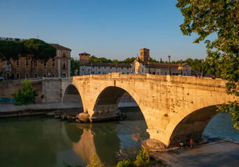 View of the Ponte Fabricio Rome, which connects the Tiber island to the Jewish quarter. The bridge reflects with shadows its arches in the Tevere river at sunset on a hot summer day.