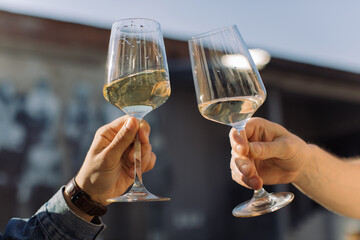 Men making celebratory toast with glasses of white wine at summer party. Golden light, relax concept.