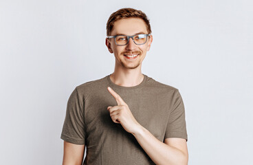 Portrait of a cheerful handsome man with a fashionable haircut and beard, smiling happily and pointing his finger at an empty advertising space on a white background.