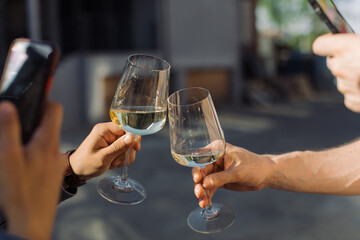 Men taking photo of celebratory toast with glasses of white wine at summer party. Golden light, relax concept.