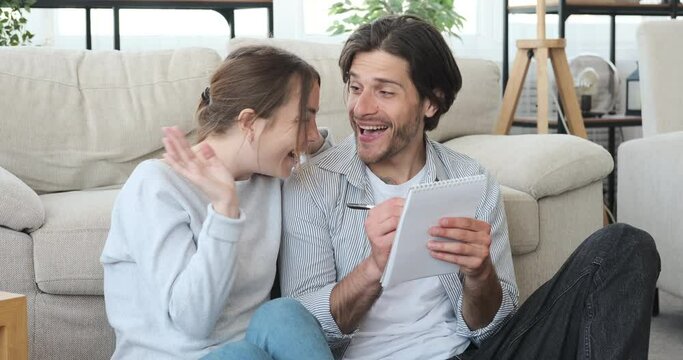 Happy couple planning and writing shopping list in notepad at home
