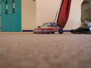 A janitorwith a vacuum cleaner in a large carpeted room