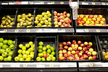 Supermarket fruit and vegetable containers displaying local produce of red and green apples,