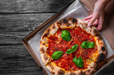 woman Hand takes a slice of Pepperoni Pizza with Mozzarella cheese, salami, Tomatoes, pepper, Spices and Fresh Basil. Italian pizza on wooden table background