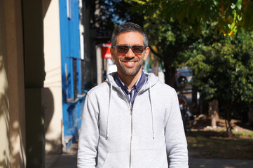  Portrait of a young man with glasses smiling to the camera and walking in the street