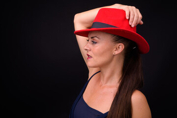 Mature beautiful woman wearing red fedora hat against black background