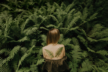 Girl's back among the ferns with wings of leaves.
