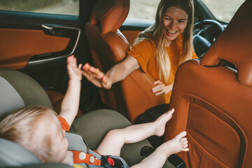 Mother with child in car on road trip high five hands baby sitting in safety seat woman driver...