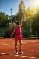 a happy girl on a tennis court lifting her tennis racket to the sky