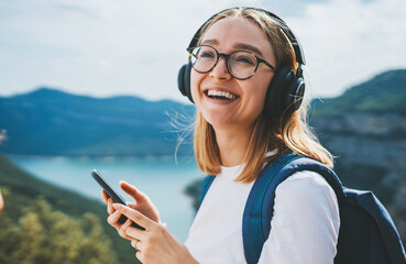 portrait smiling traveler woman with glasses holds smartphone device in hands and listens music for...