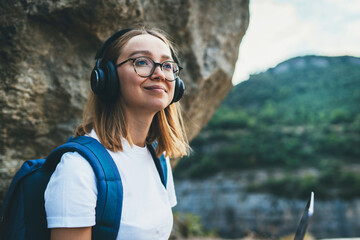 young female student looks up in hipster glasses and wireless headphones enjoys nature in the mountains while Hiking walk, freedom concept