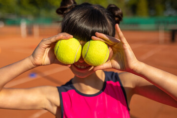 fun girl playing with two tennis balls outdoors on a tennis court