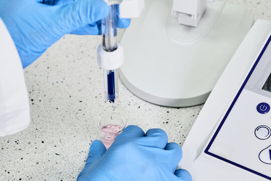 Woman in a rubber gloves holding a glass electrode for measuring of pH of the solution using pH meter. Analytical or electro chemistry laboratory. 