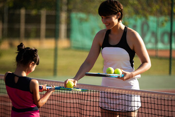 a mother and daughter playing tennis together outdoors on a clay court