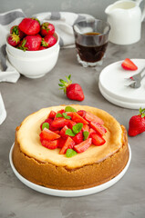Homemade cheesecake New York with fresh strawberries on a white plate with coffee on a gray stone background. American cuisine.