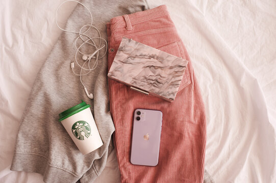 Moscow/Russia - July 23, 2020: Iphone 11 In Purple Shade With Starbucks Coffee Cup And Stylish Bag On Clothes In Bed Closeup. Top View.