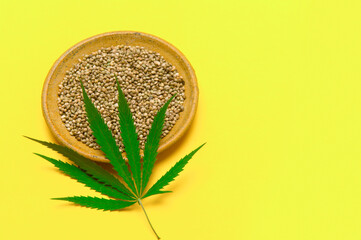 Green cannabis leaf and seeds on plate on yellow background. Vegetarian food concept.