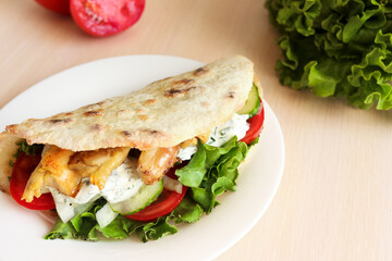 Sandwich wrap with meat and vegetables on white plate,