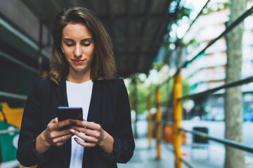 Fototapeta premium Woman listens to music with wireless headphones walking outside in city and using in hand smartphone, businesswoman typing on touch screen of cellphone while internet technology outdoors
