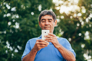 Man in his seventies using smartphone outdoors