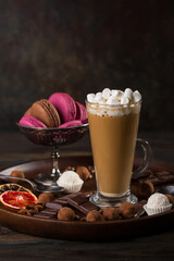 A glass of coffee latte with cakes and truffles on a dark background.