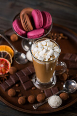 A glass of coffee latte with cakes and truffles on a dark background.