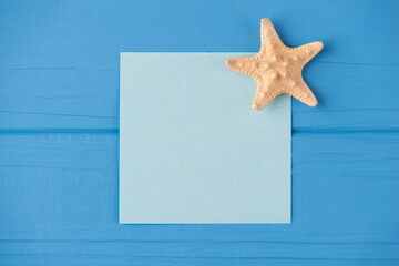 Fototapeta na wymiar Top above overhead view close-up photo of a blank note with a small starfish isolated on blue wooden background with copyspace