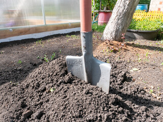 A garden shovel in the excavated earth against the background of garden buildings.