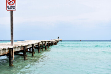 Man walking along wooden pier over the bright blue water