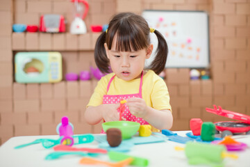 toddler girl pretend play food preparing role against cardboard blocks kitchen background