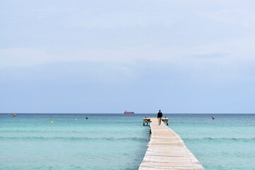 Man walking along wooden pier over the bright blue water