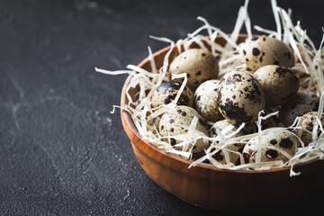 Wooden bowl with straw and quail eggs on the black concrete background. Flat lay