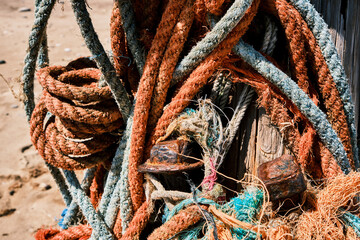Vibrant weathered and worn ropes hang off a wooden sea defence post with rusty pegs on Spurn Head, England